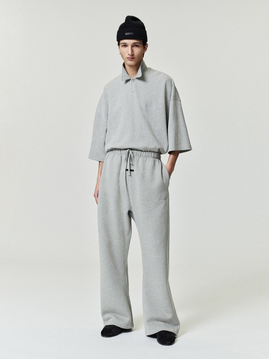 man in light grey relaxed fit sweatpants with elastic waistband and matching loose short sleeve top wearing black beanie