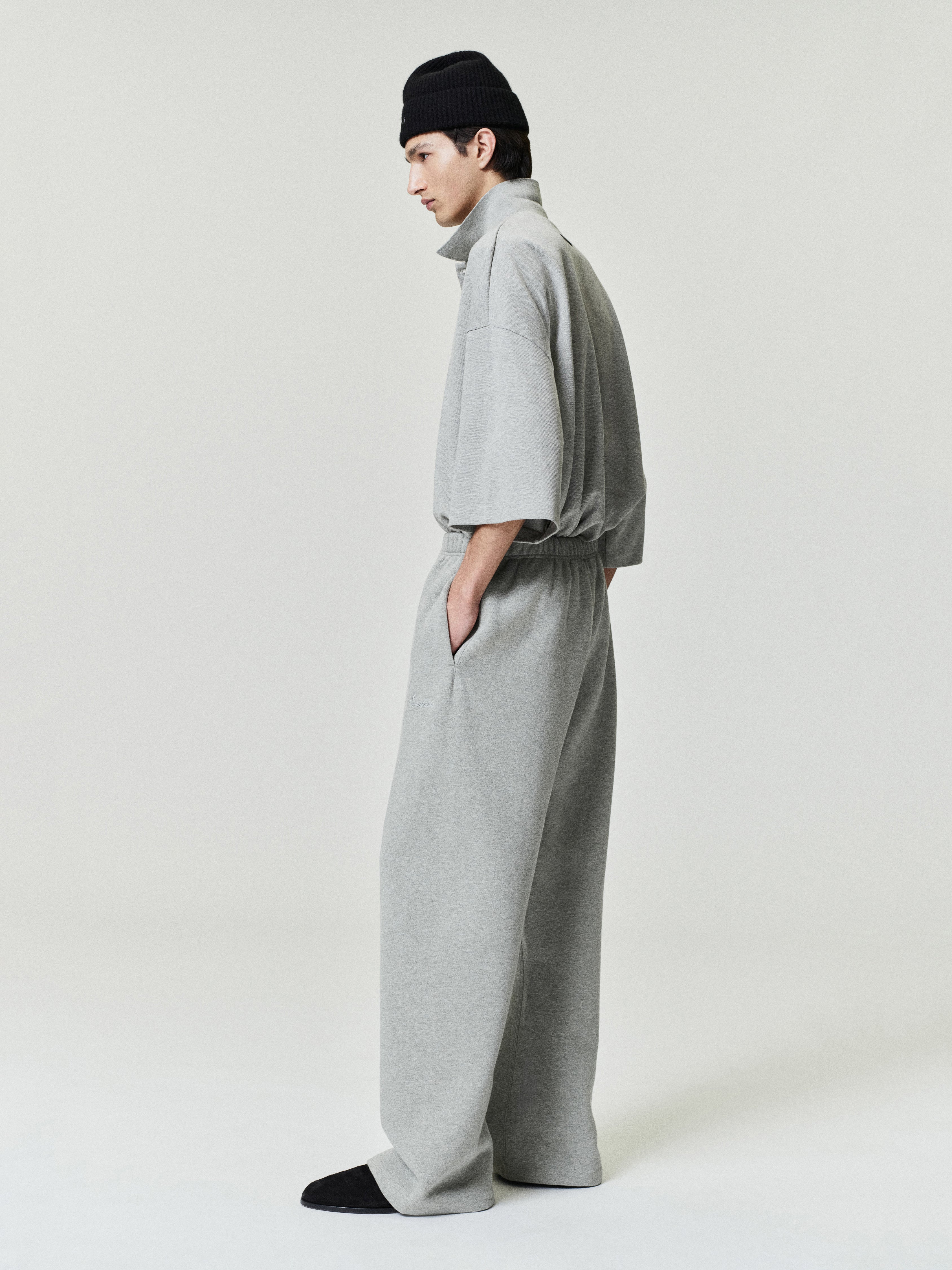 man wearing light grey relaxed fit flare sweatpants paired with matching oversized short sleeve top and black beanie