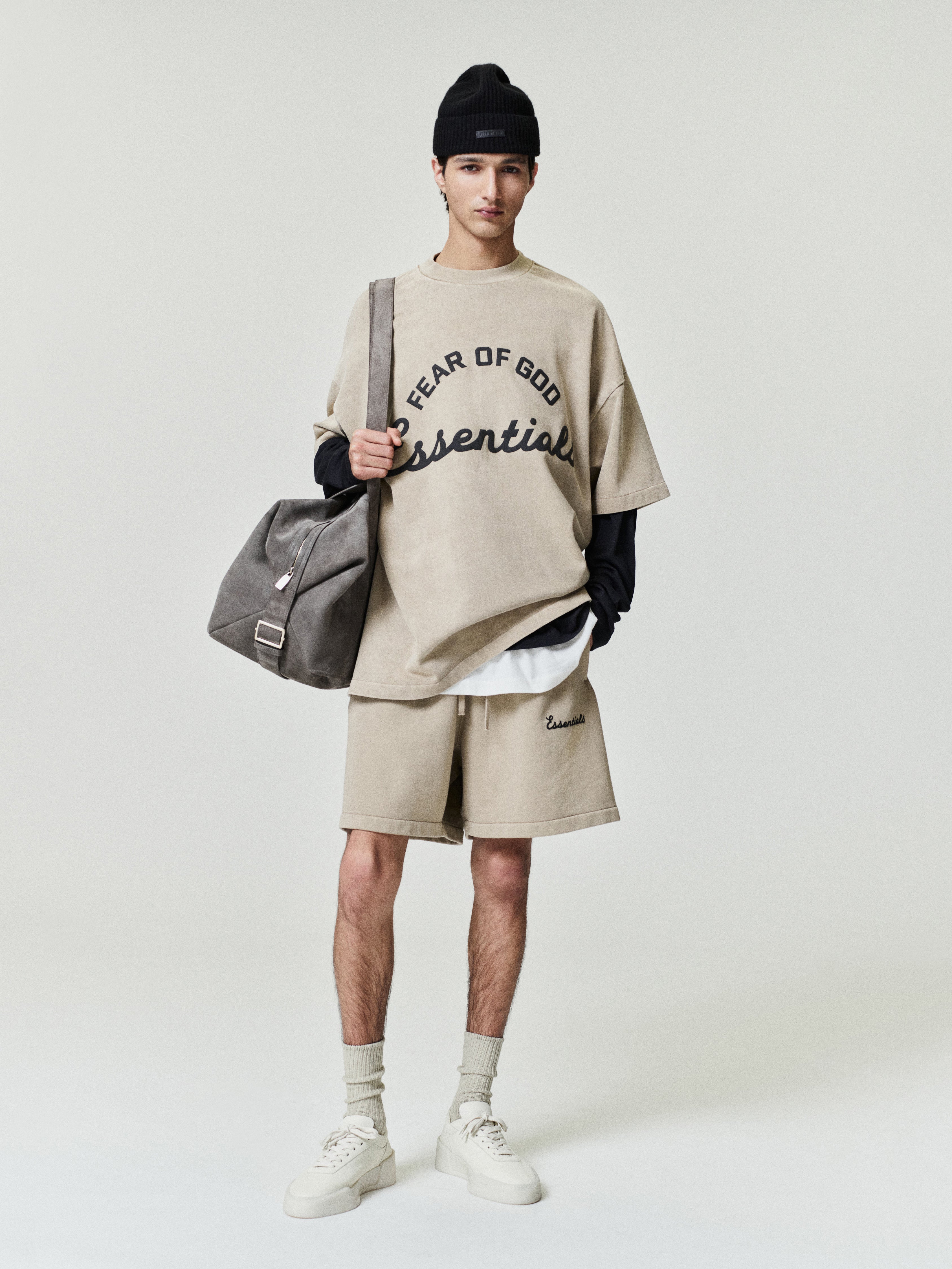 male model wearing oversized pigment-dyed beige 90s fit Fear of God Essentials short sleeve tee with shorts and black beanie