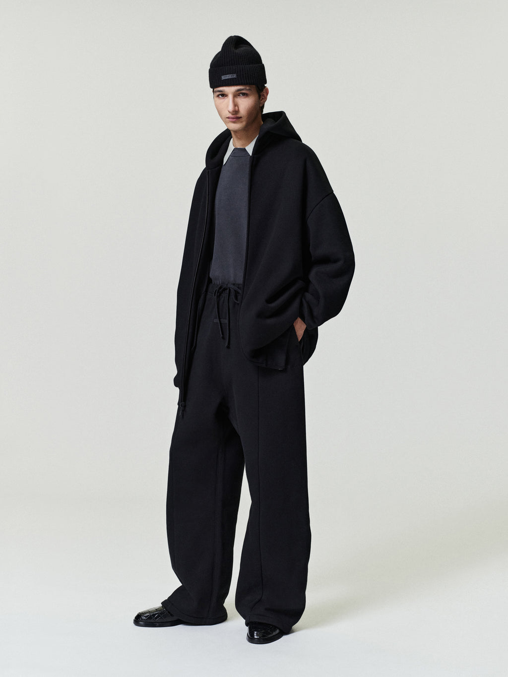 man wearing relaxed fit black canvas pleat front pants with elastic waistband and loose black jacket