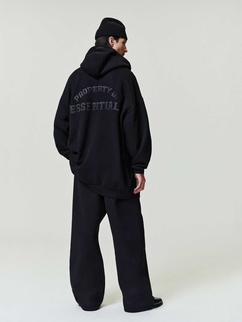 man in oversized black hoodie with graphic text paired with loose black pleated pants and black beanie