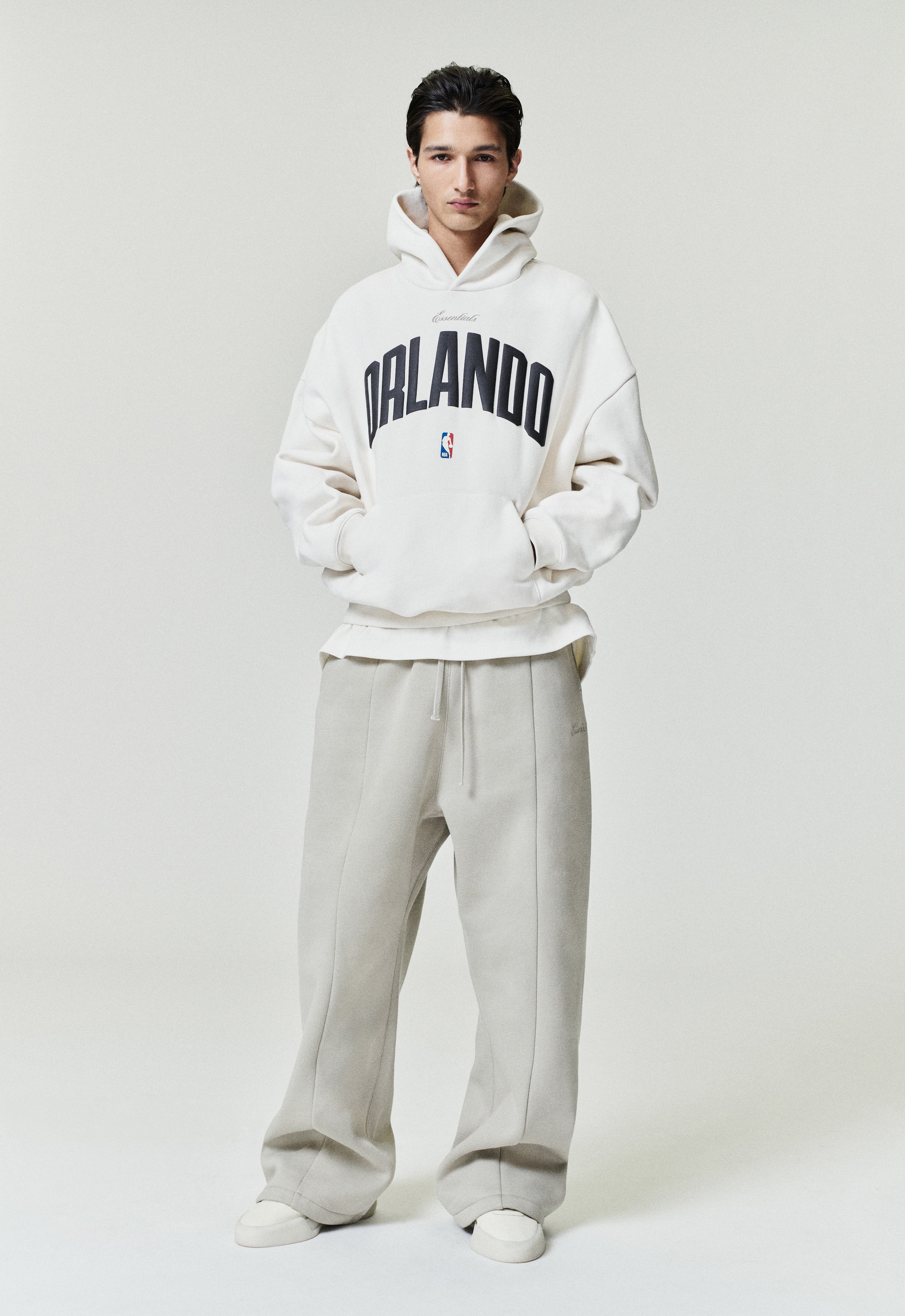 Front view of model wearing off-white Orlando Magic 90s Hoodie with black Orlando text and small NBA logo, image SP26_F_L64-P_3090