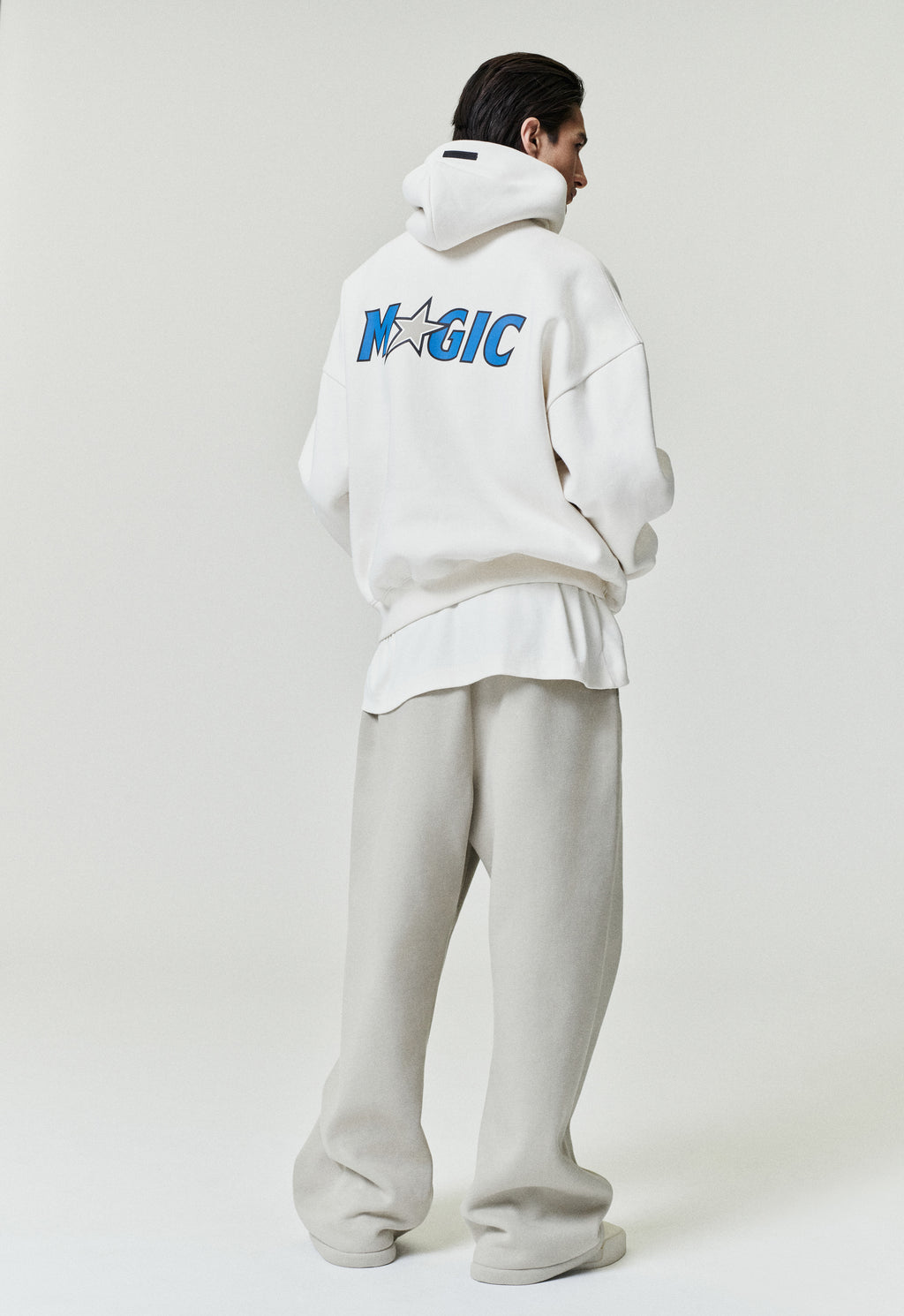 Rear view of white Orlando Magic 90s Hoodie with blue team logo and star detail, model standing, image SP26_F_L64-P_3121
