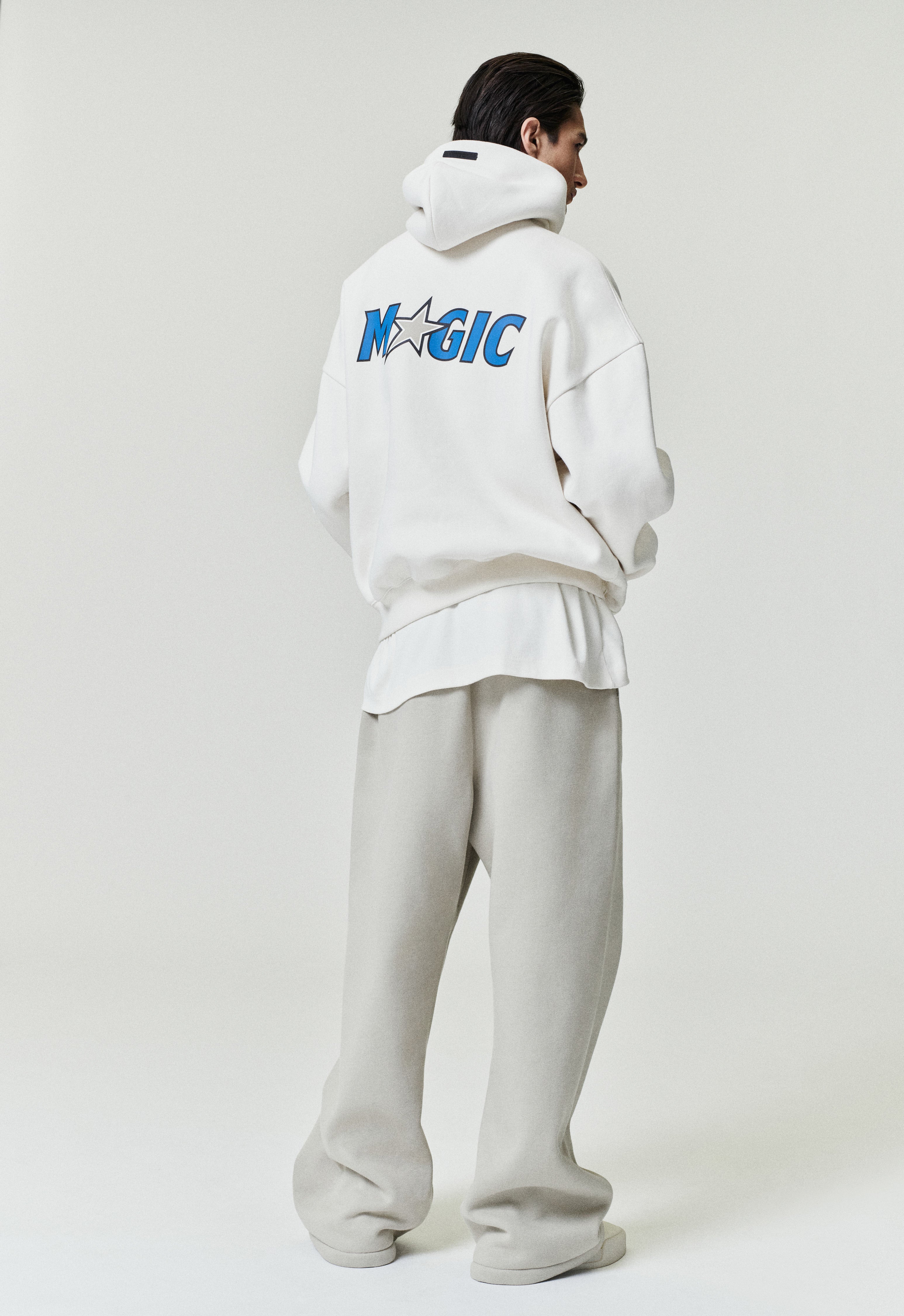 Rear view of white Orlando Magic 90s Hoodie with blue team logo and star detail, model standing, image SP26_F_L64-P_3121