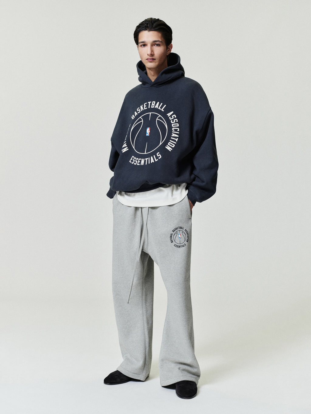 navy oversized hoodie with circular NBA Essentials text and basketball graphic worn with gray sweatpants with matching logo