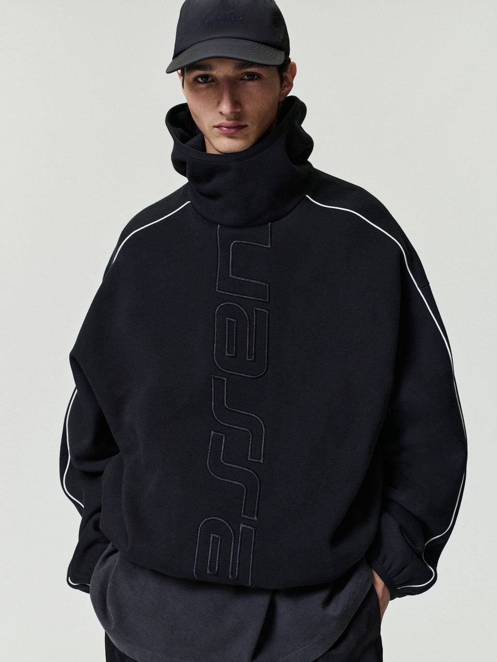 Person wearing a black hoodie with branding on a plain background