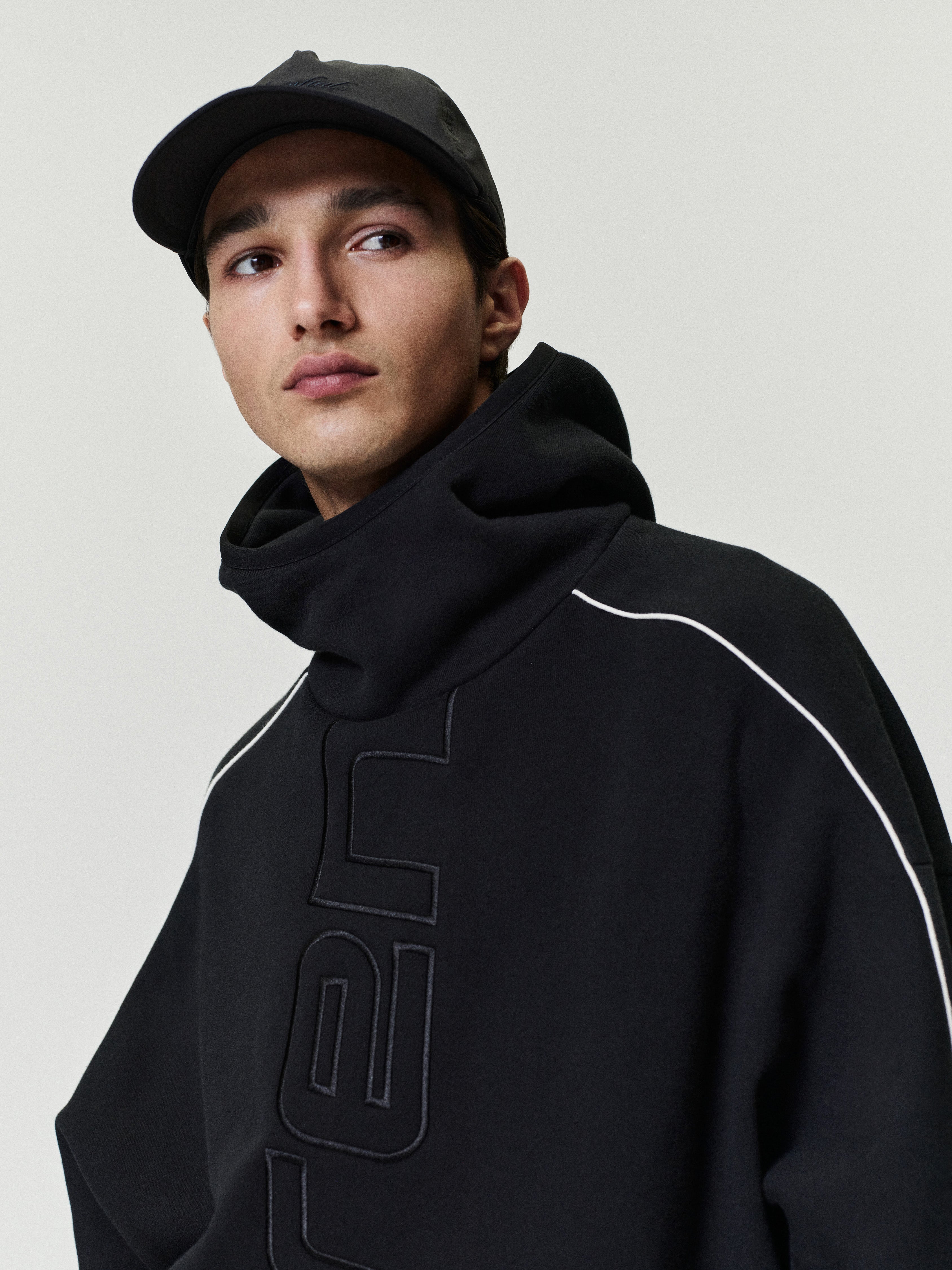 Person wearing a black hoodie with a logo on a plain background