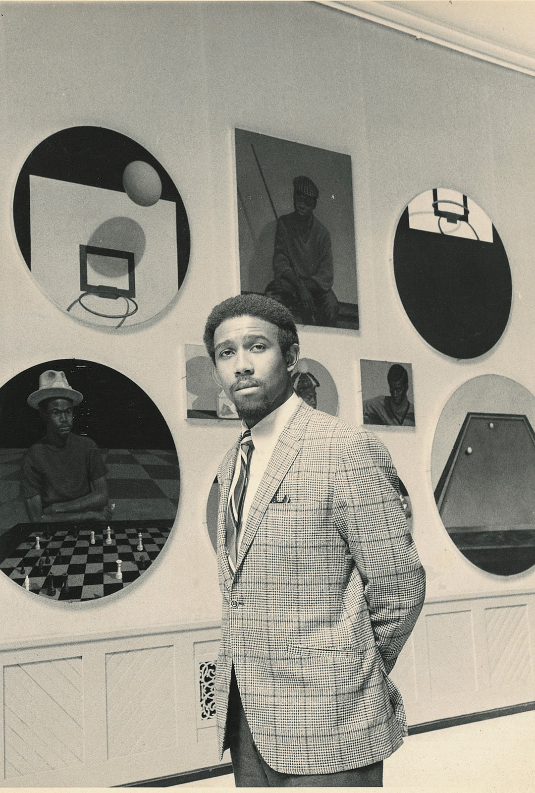 Man in a checkered suit standing in front of circular portraits on a wall.