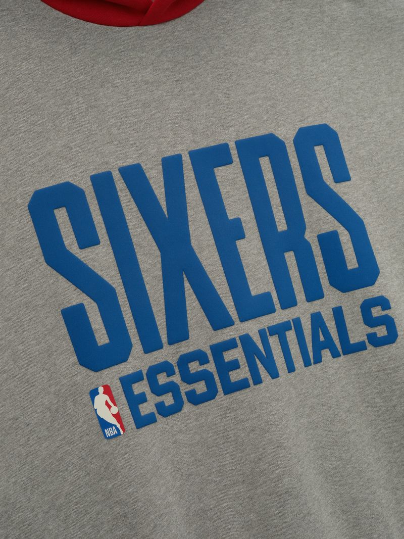 Close-up of grey Sixers Sport hoodie front with large blue SIXERS ESSENTIALS text and small NBA logo below