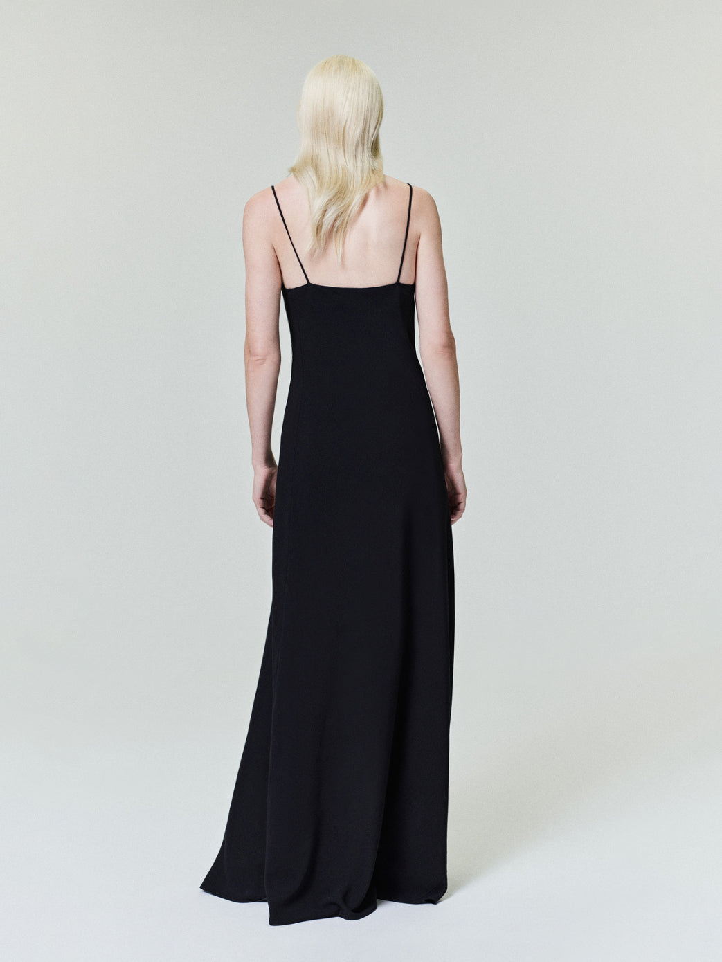 Back view of a model wearing a sleek black Womens Viscose Slip Dress with thin straps and a flowing silhouette against a simple neutral backdrop.