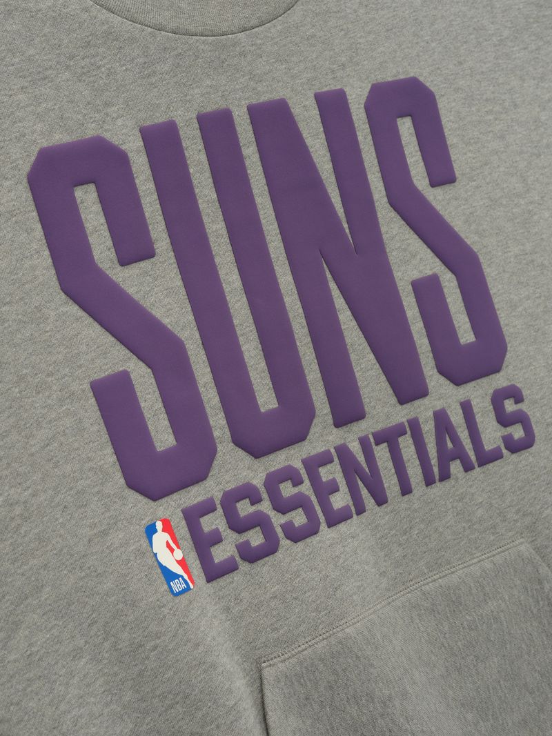 Close-up of grey crewneck with large purple SUNS lettering and smaller ESSENTIALS text above kangaroo pocket and NBA logo patch